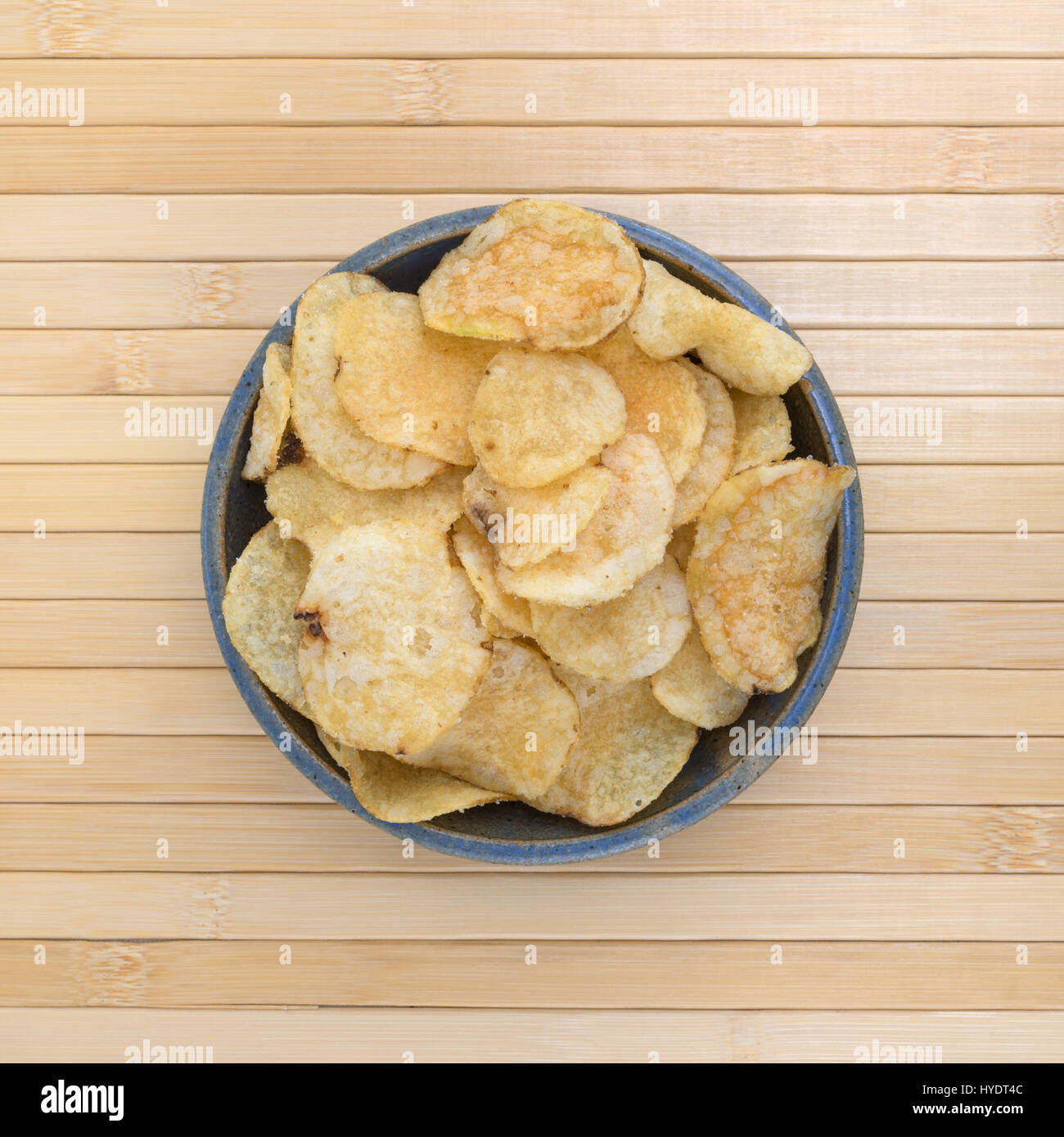 Top view of an old stoneware bowl filled with salt and vinegar flavored potato chips on wood place mat. Stock Photo