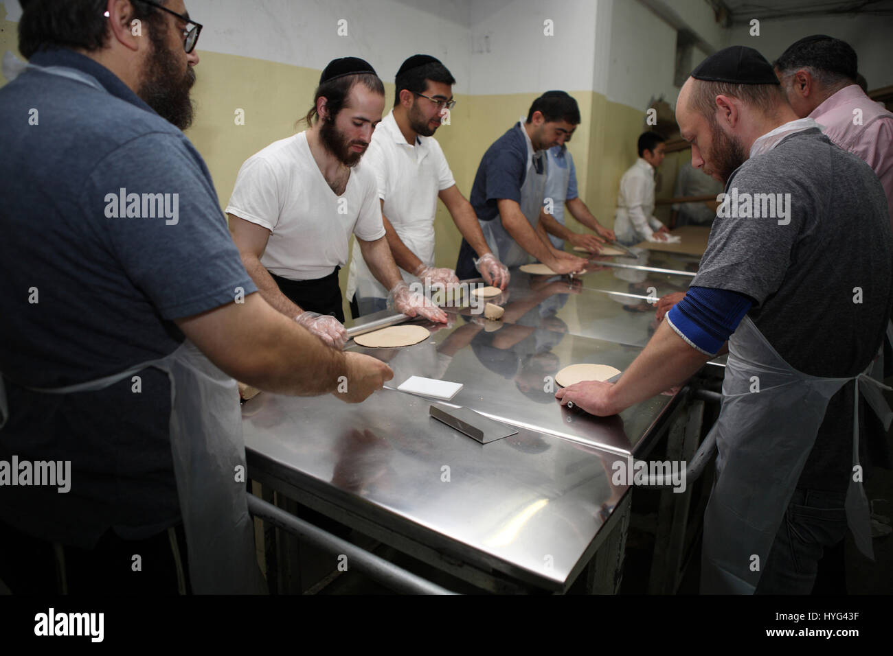 Religious Jewish men use rolling pins to flatten pieces of dough before they are put in the oven to make Matza or Matzah Shmura for Passover Stock Photo