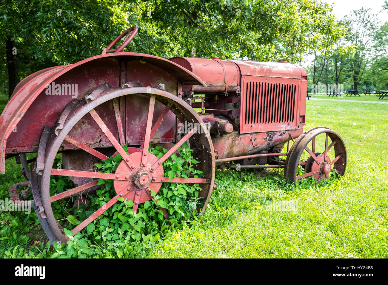 An old rusty red tractor with metal wheels sits in a field of green pasture in Ontario Canada. Stock Photo
