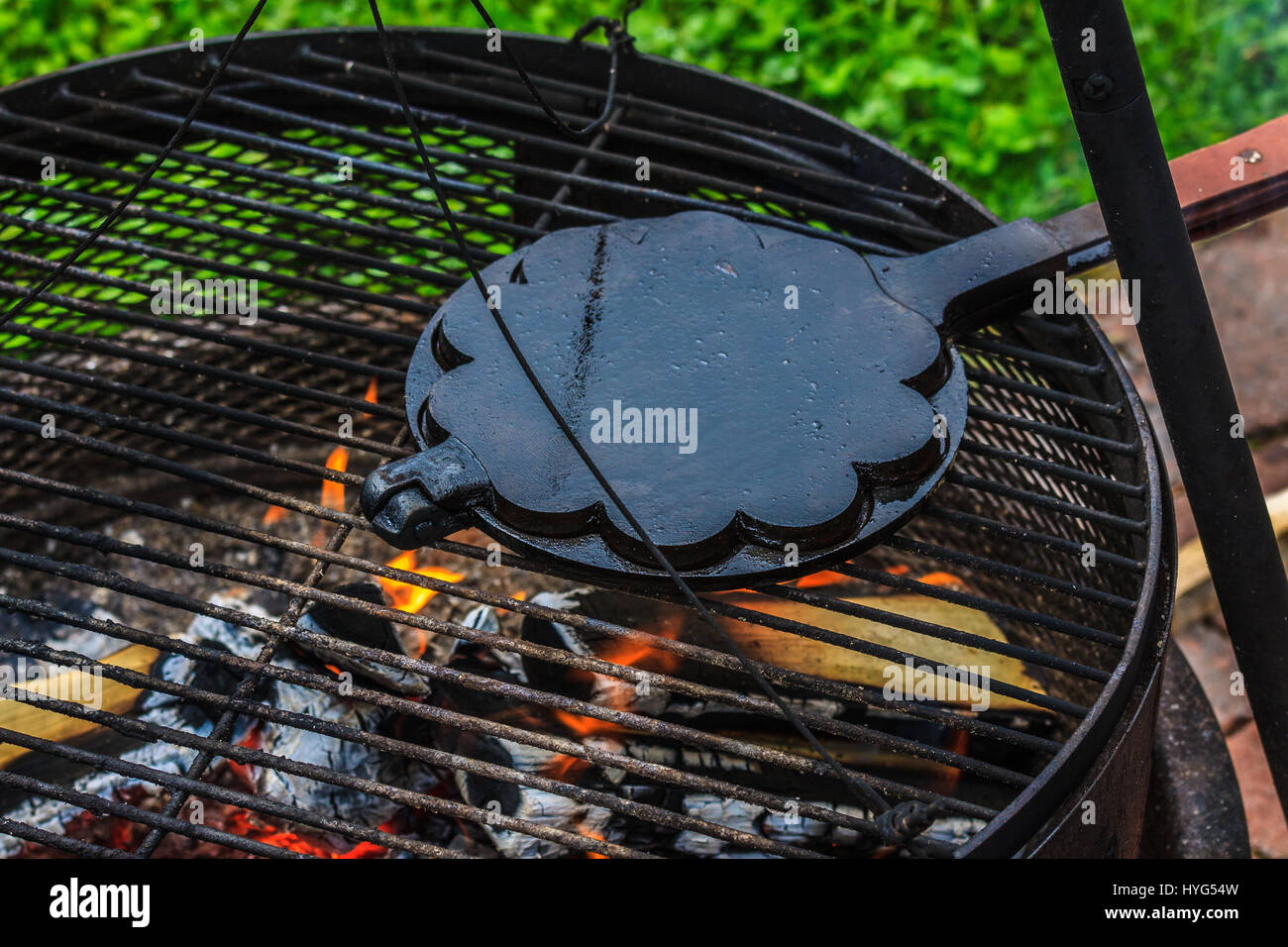 Old cast-iron waffle iron, baking waffles on open flame grill outdoors. Stock Photo