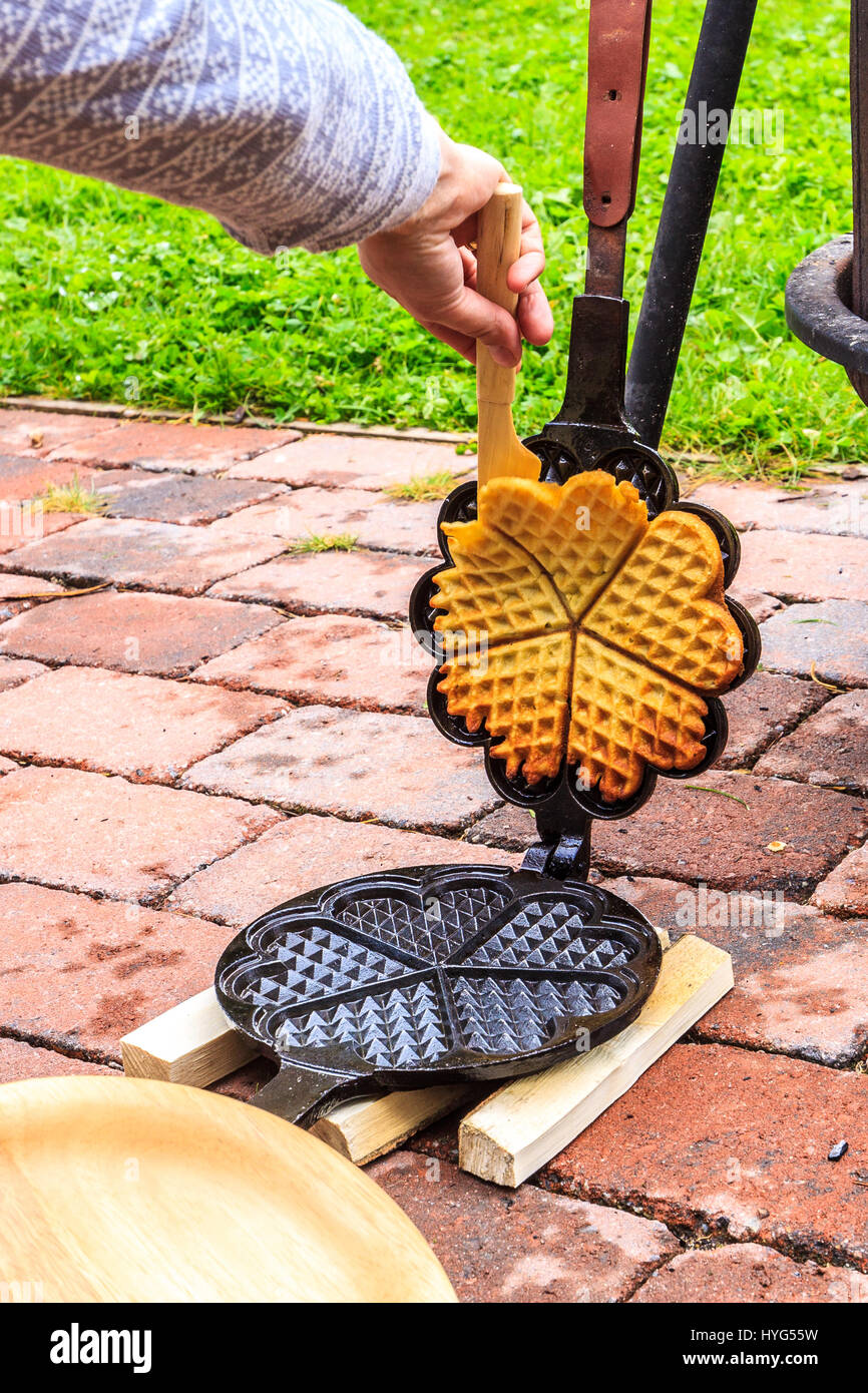 Fresh baked waffle being taken out of cast-iron waffle iron. Visible female hand. Stock Photo