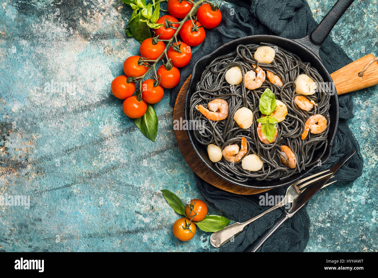 Black spaghetti with prawns and scallop in frying pan on blue background, top view with copy space Stock Photo