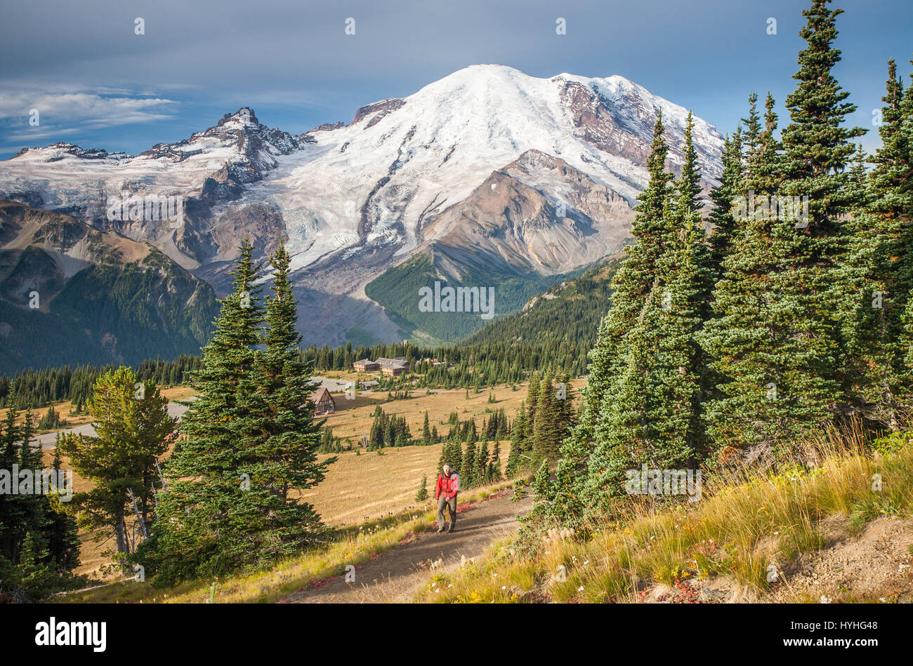 Hiker on Sourdough Ridge with Mount Rainier and Sunrise Lodge in background. Stock Photo