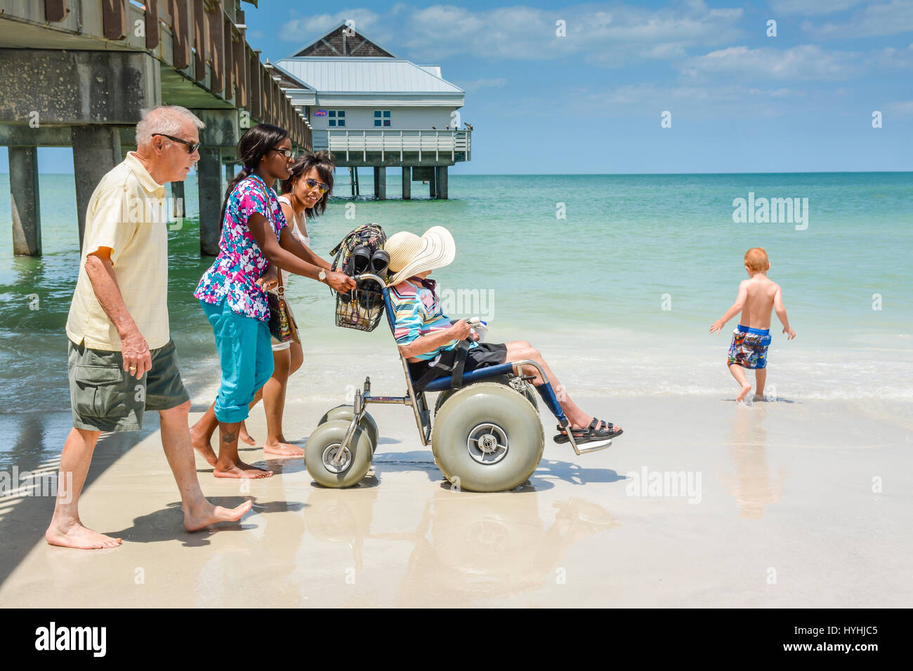 Side View of disabled woman being pushed in beach wheelchair at shoreline by African American