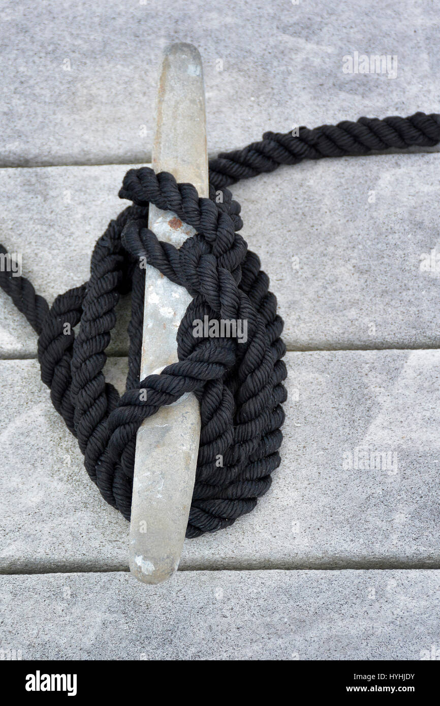 A close up view of a cleat hitch type of nautical knot made of black rope moors an unseen boat to the dock Stock Photo