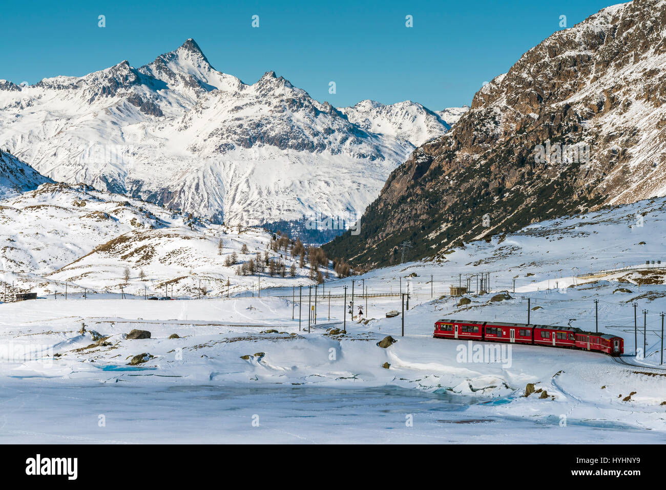 Bernina Express red train passing Lago Bianco in a scenic winter mountain landscape, Graubunden, Switzerland Stock Photo
