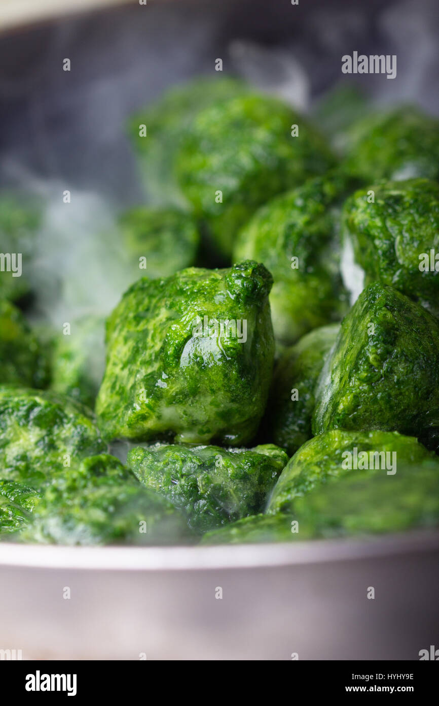 Frozen nice and green briquettes of spinach are being cooked on a pan. Stock Photo
