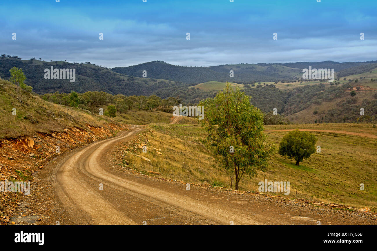 Narrow dirt road winding through vast  landscape of forested hills and valleys of Great Dividing Range under blue sky in NSW Australia Stock Photo