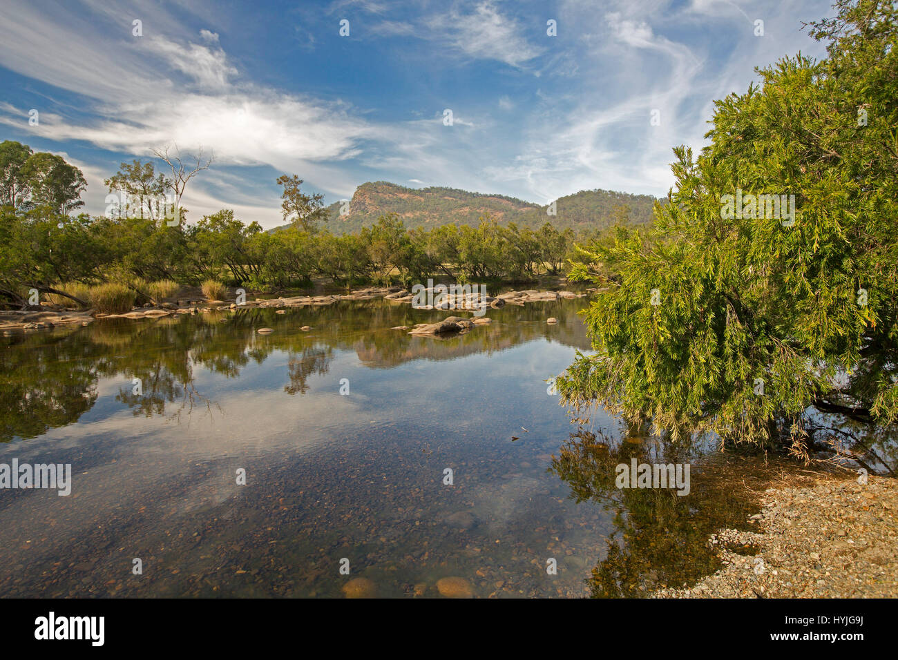 Mann River hemmed with forests & with peaks of ranges on horizon with blue sky & clouds reflected in mirror surface of  water, Coombadja NSW Australia Stock Photo