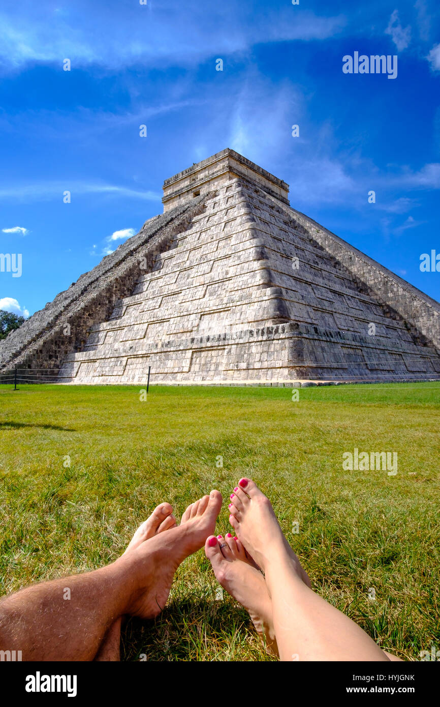 Pyramid Castillo in Chichen itza and legs of couple relaxing on grass, Mexico Stock Photo