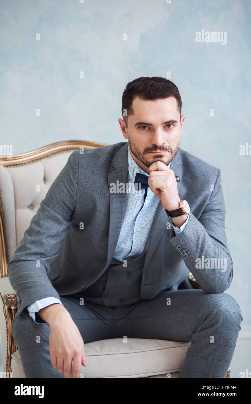 Portrait of a beautiful adult man in a gray suit sitting in a chair in ...