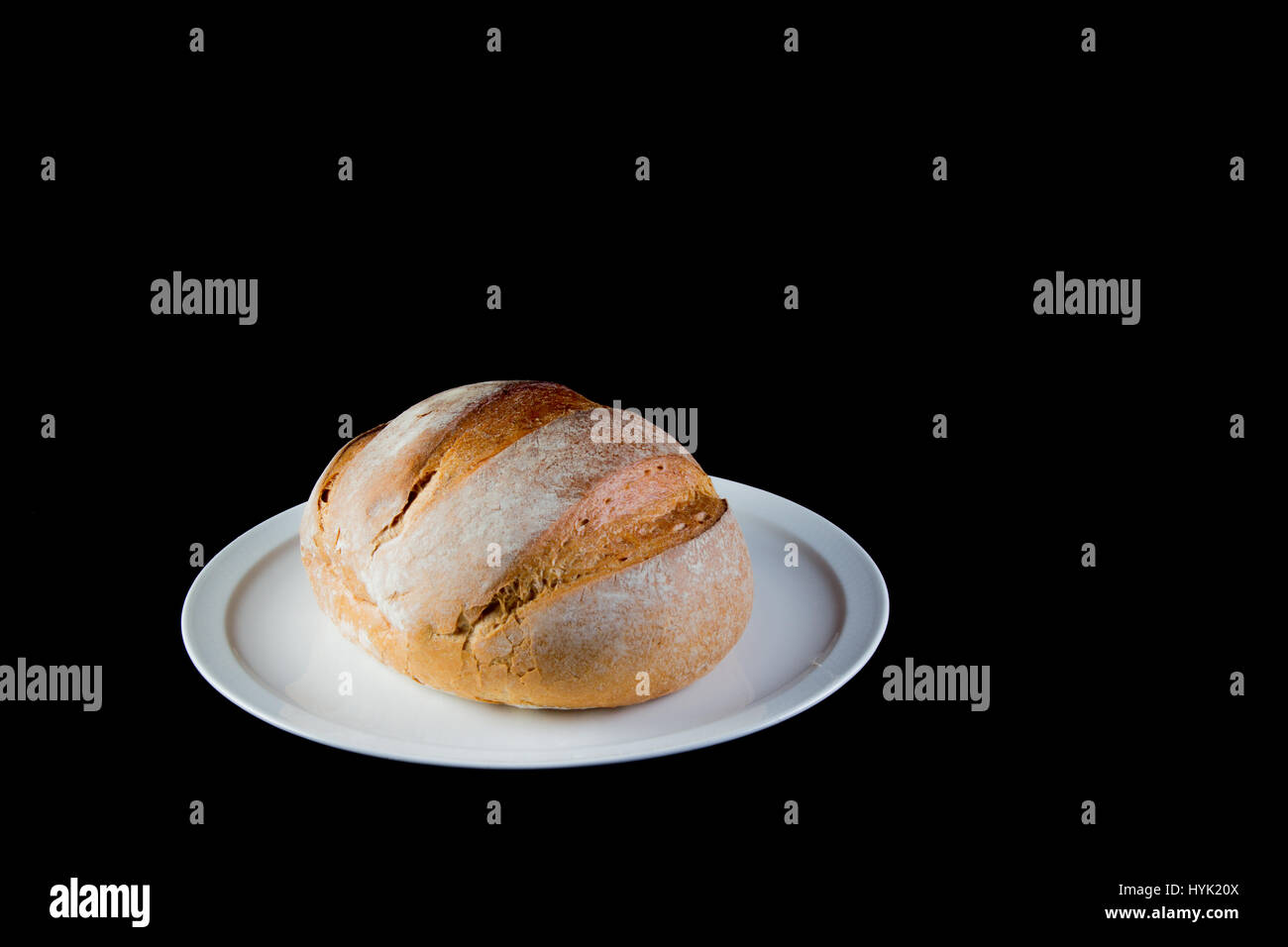 Full rustic loaf of bread on a white dish isolated on black background Stock Photo