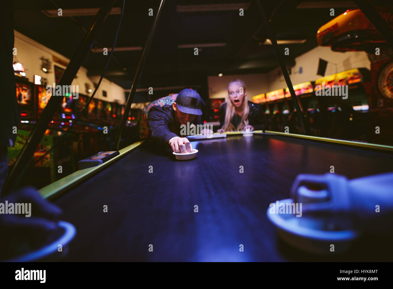 Happy young friends playing air hockey game at amusement park. Man hitting puck with striker. Stock Photo