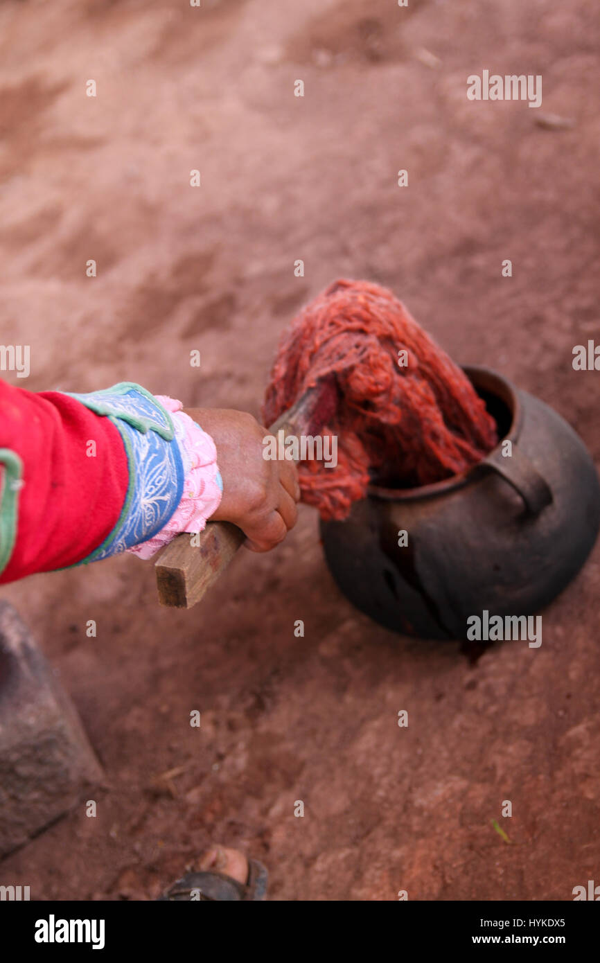 Peruvian woman in traditional clothing using a stick and ochre pot to dye alpaca yarn with natural dyes from vegetables and plants. Stock Photo