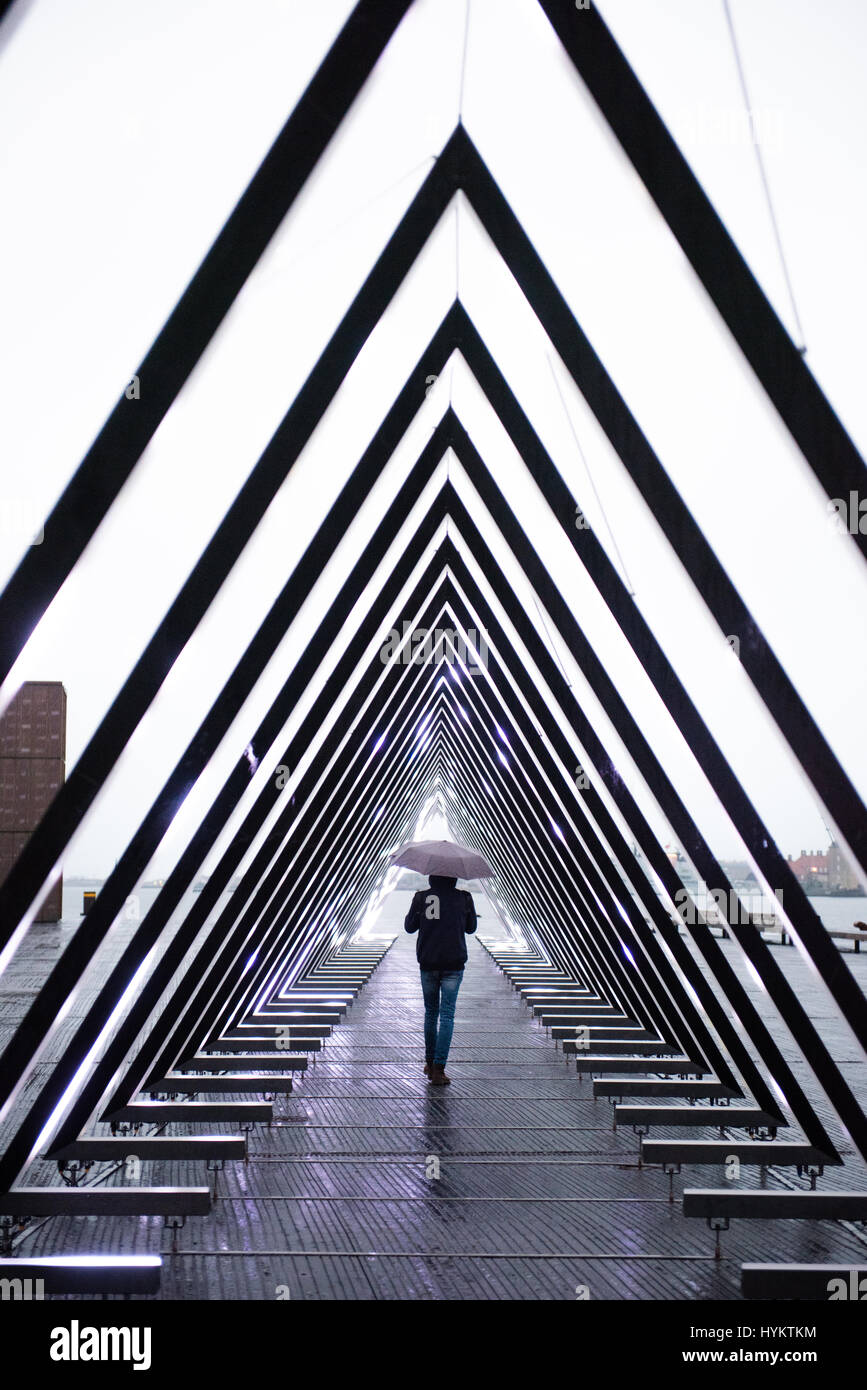 A young man walk under an umbrella around a modern art piece with dynamic lights and sound by the new Opera House in Copenhagen's harbourside Stock Photo