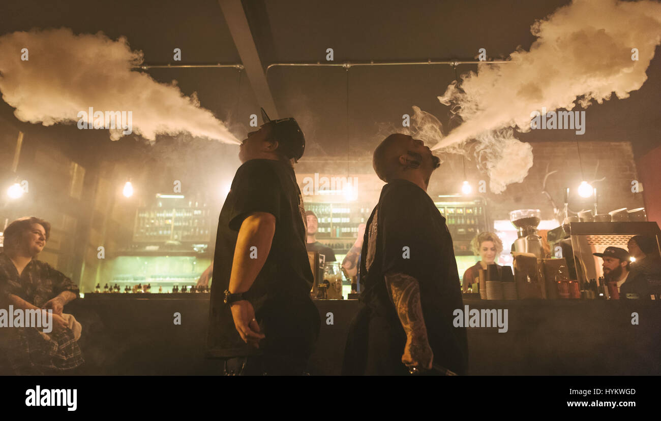 LONDON, UK: A pair of vapers breath out the gaseous plumes. LIFTING the lid on UK underground vaping culture these pictures show how this craze is set to take hold of the nation. Huge plumes of vapour can be seen bellowing out of the mouths and noses of the hipsters of the Capital – known collectively as “vapers” who now number nearly three million in total across Britain. London-based photographer Louis Amore (43) happened upon this vape café in Hoxton by chance and was inspired to photo-document this emerging craze. Stock Photo