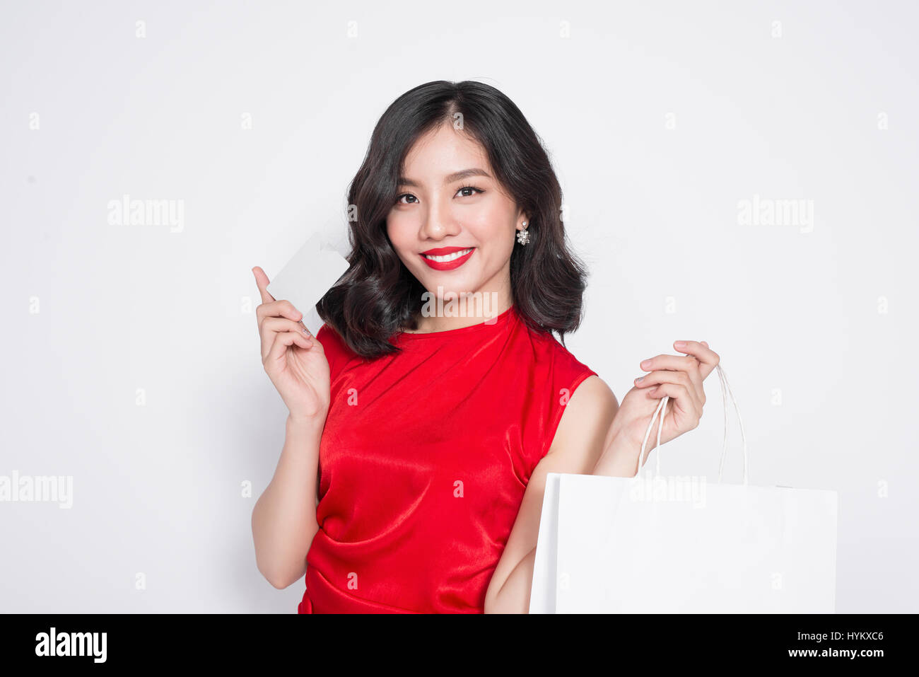Beautiful asian woman wearing a red dress with shopping bag and holding credit card standing over white. Stock Photo