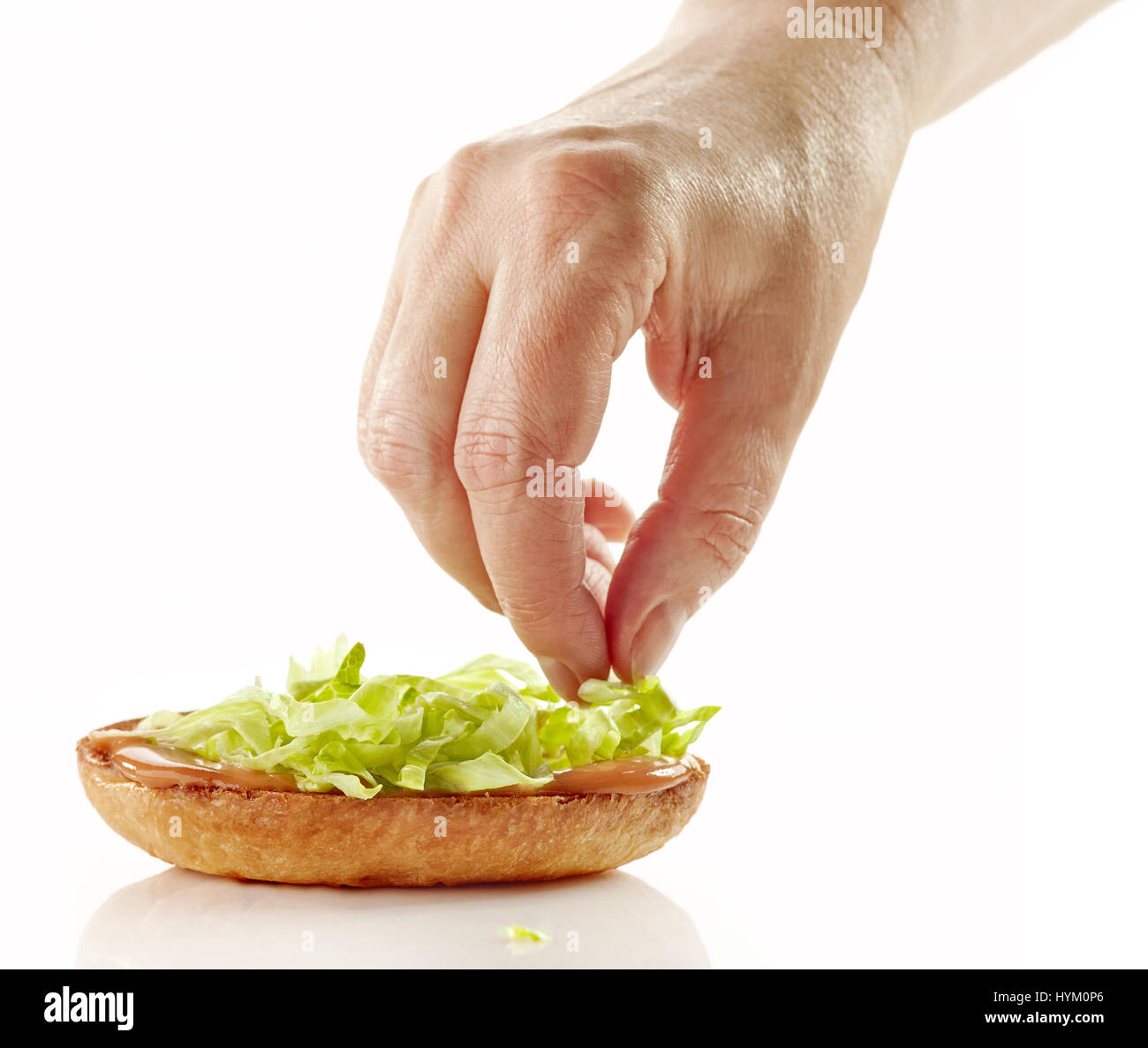 cook adding a lettuce on burger bun, process of making hamburger on a