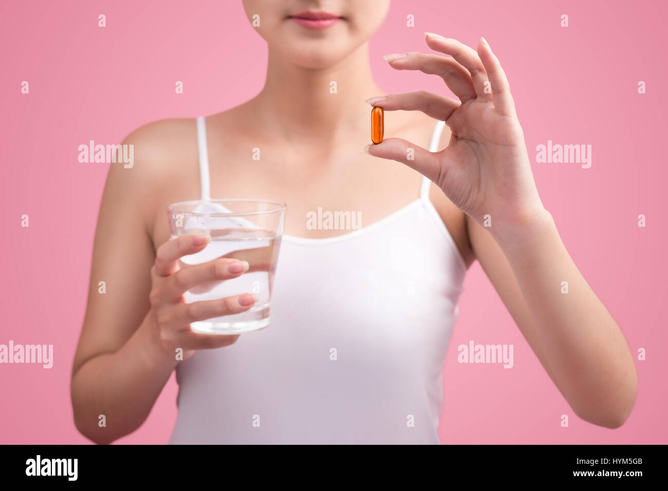 Young asian beauty young woman eating pills and drinking water on pink background. Stock Photo