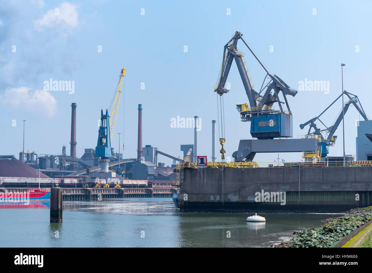 harbor crane unloading a ship in front of a large steel factory Stock Photo