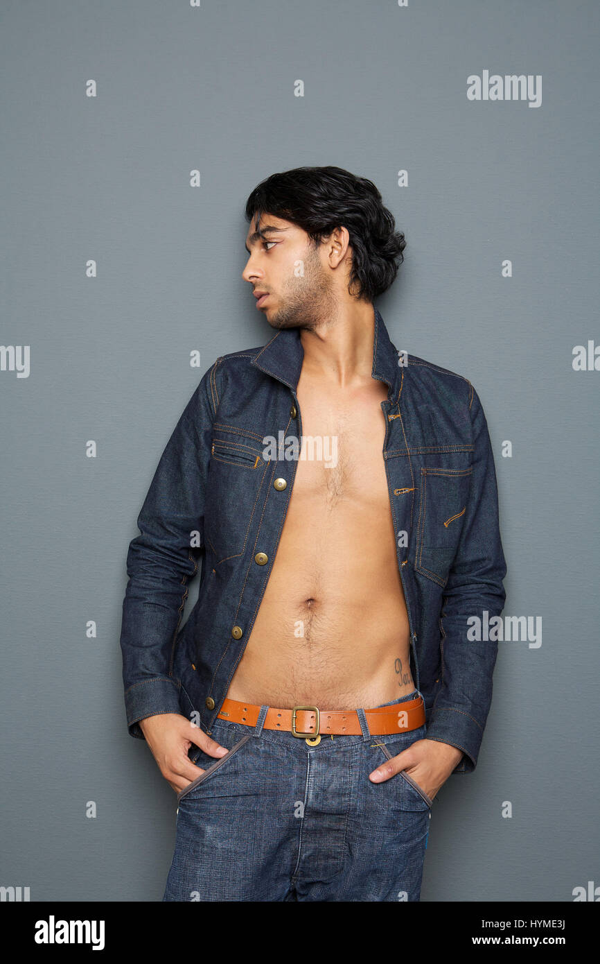 Portrait of a man looking away with open shirt standing against gray background Stock Photo