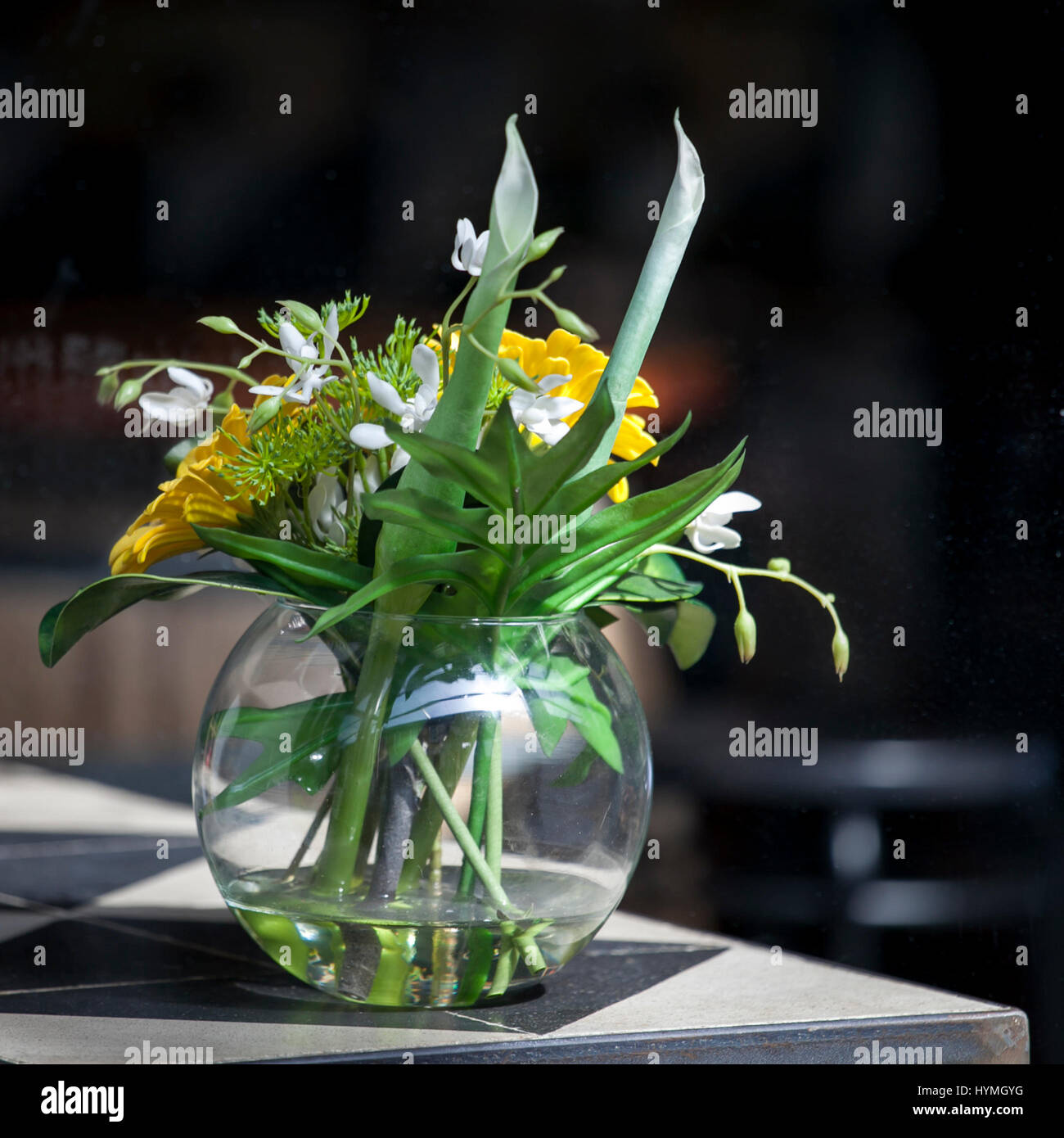 Artificial bouquet of leaves of monstera Alismatales , gerbera Transvaal daisy and sunflower in the glass vase on the table Stock Photo