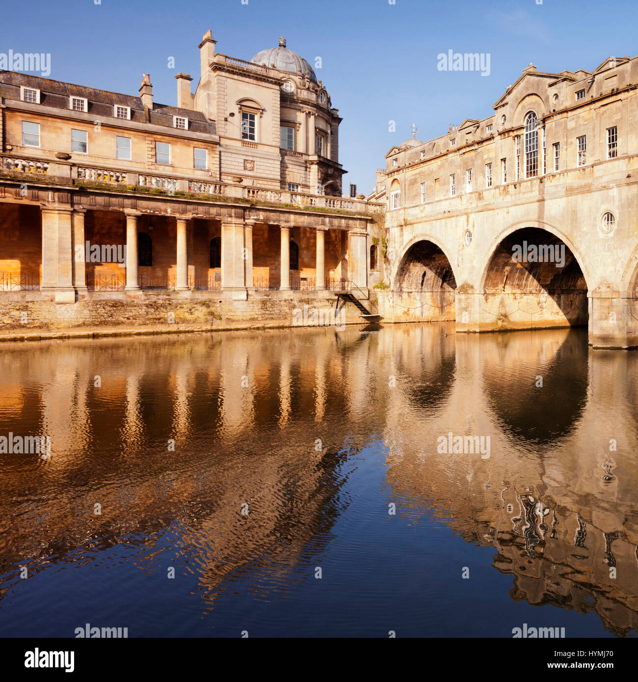Pulteney Bridge and Colonnade, Bath, England, on a bright spring morning, reflected in the River Avon. The bridge was designed by Robert Adam and comp Stock Photo