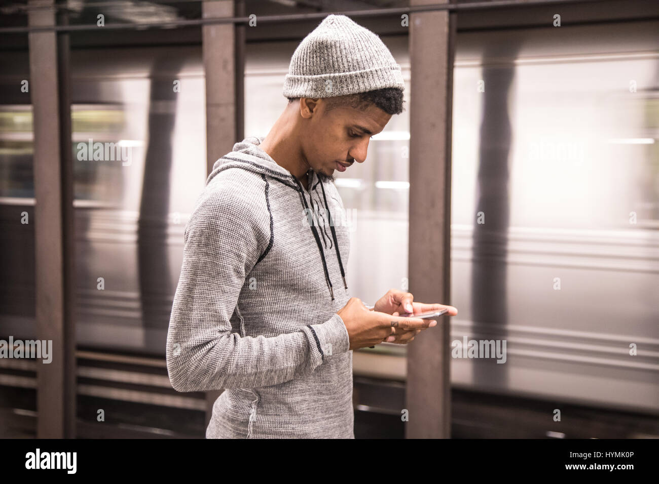 A young man texts while waiting for a NYC subway train. Shot during the Autumn of 2016 Stock Photo