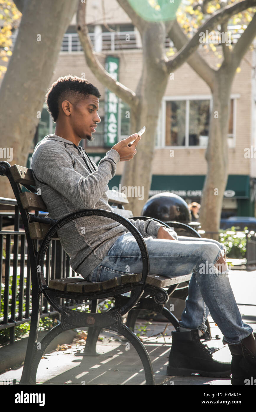 A young man scrolls through his phone while waiting in a park Stock Photo