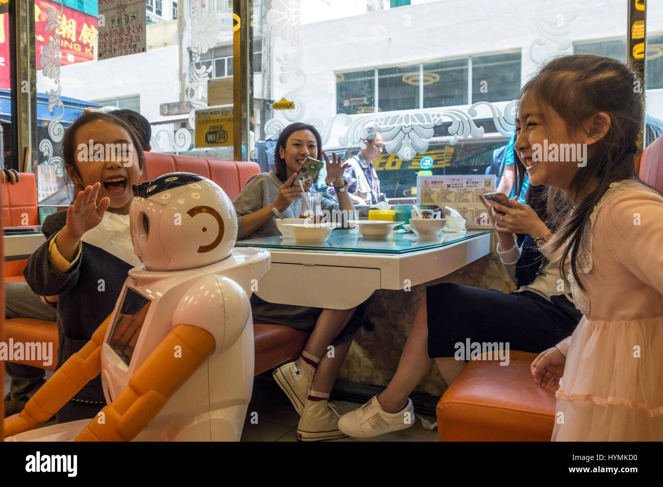 Girls interacting with robot waiter at a restaurant in Hong Kong while mother looks on Stock Photo