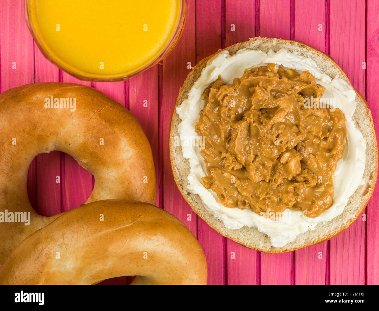 Cream Cheese and Crunchy Peanut Butter Spread Bagel Against a Pink