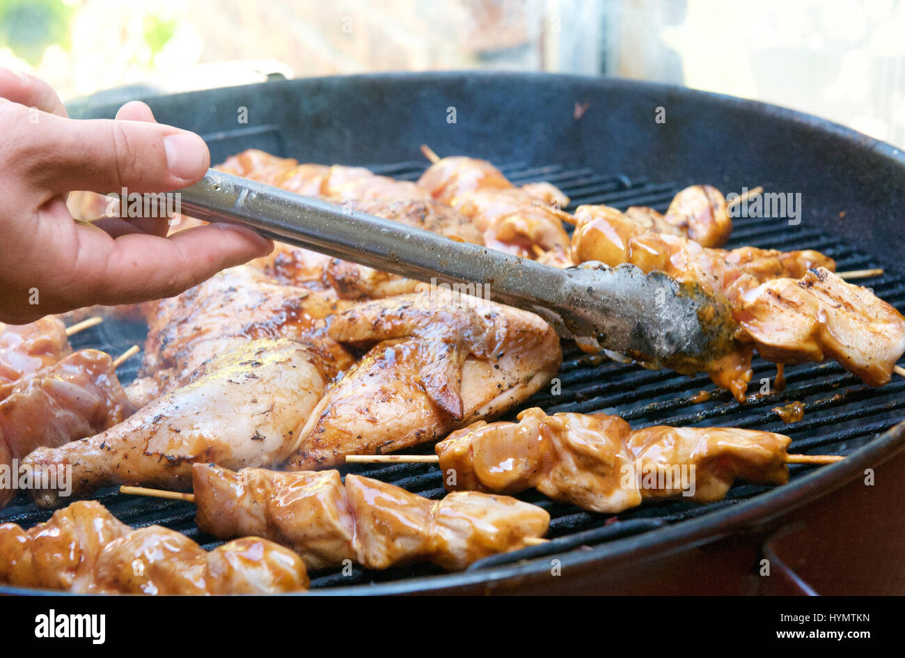 Hand holding tongs to turn over barbecue chicken Stock Photo