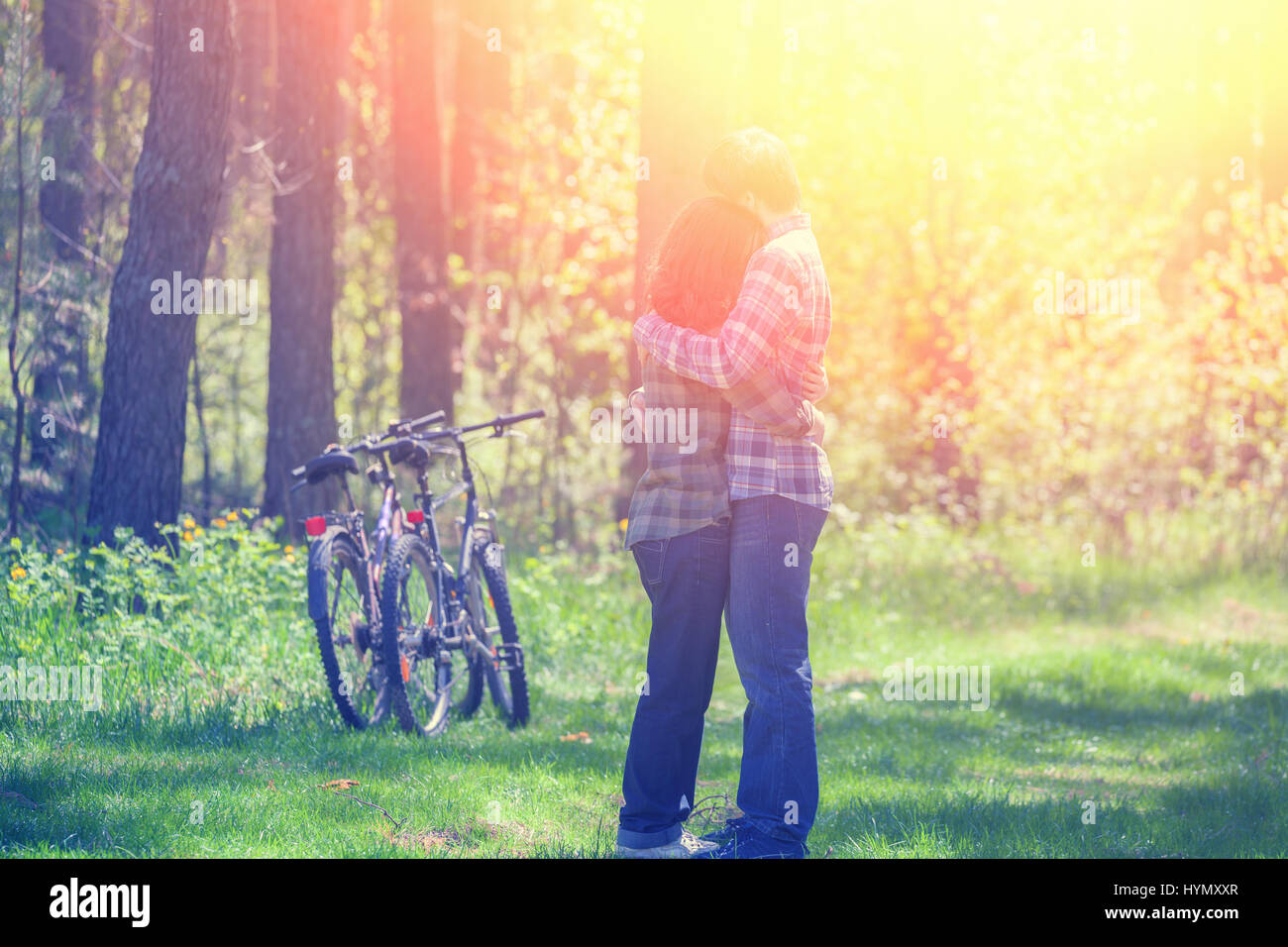Young happy couple in love hugging in the forest near two bicycles. Summertime, sunny weather Stock Photo