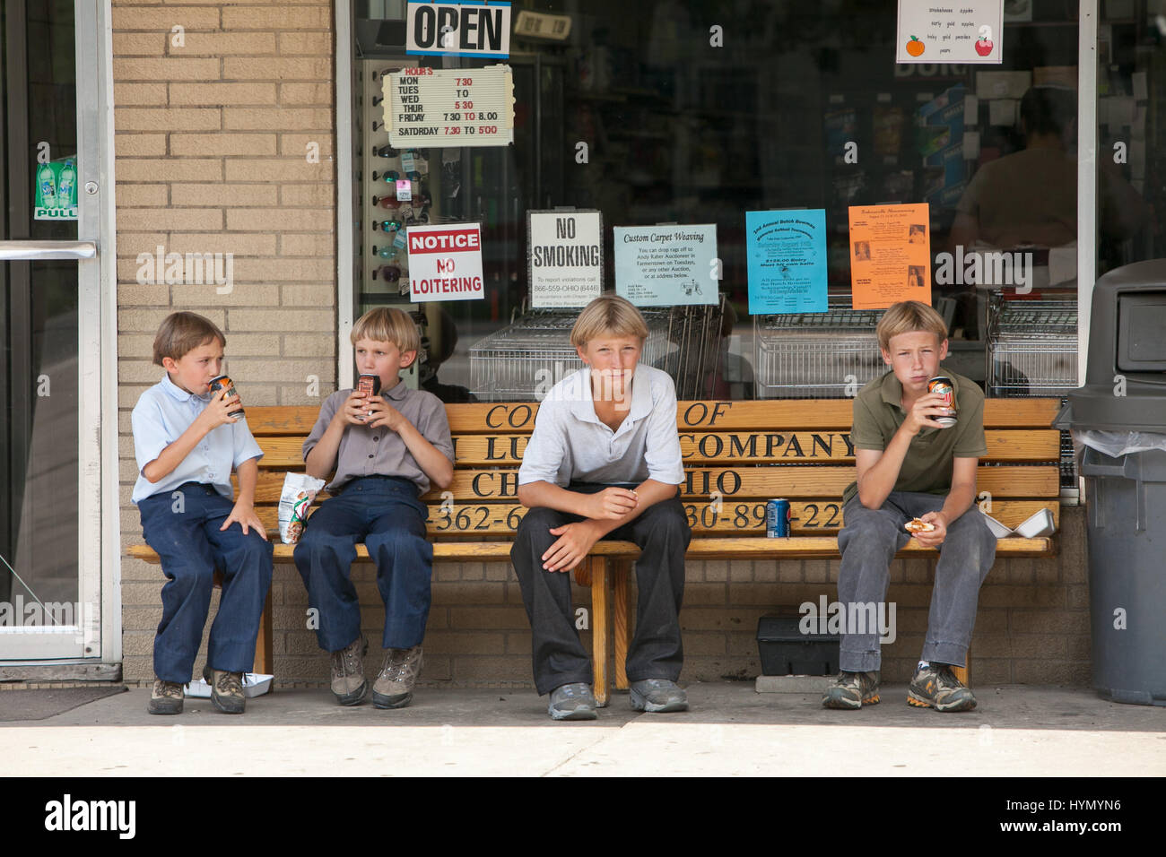 Four Amish boys eat snacks on a bench outside of a convenience store