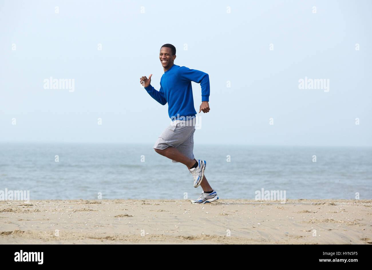 Smiling young man jogging at the beach Stock Photo