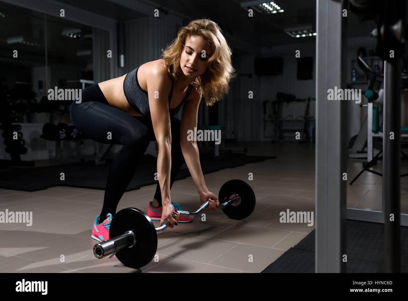 Young blonde girl in black clothes performing dead lift barbell exercises Stock Photo