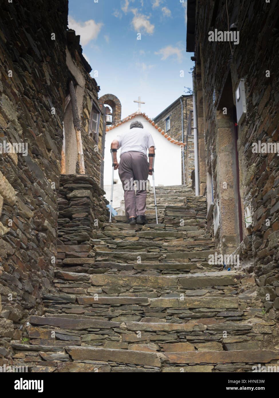Old age man with walking crutches climbing stone pathway in Portugal