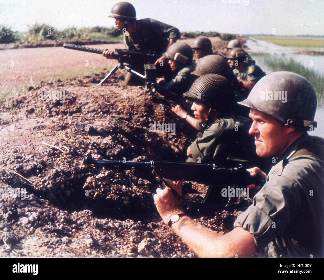 U. S. Army Advisors and Vietnamese infantrymen await attack along the bank of a rice paddy. Vietnam, 1965. . Stock Photo