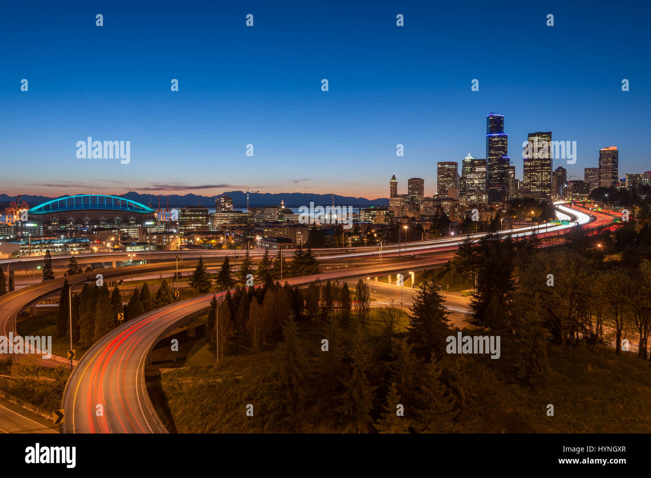 Seattle Skyline at dusk with freeway approaching the city with Interstate 90 and 5 filled with the light trains of moving traffic coming and going Stock Photo