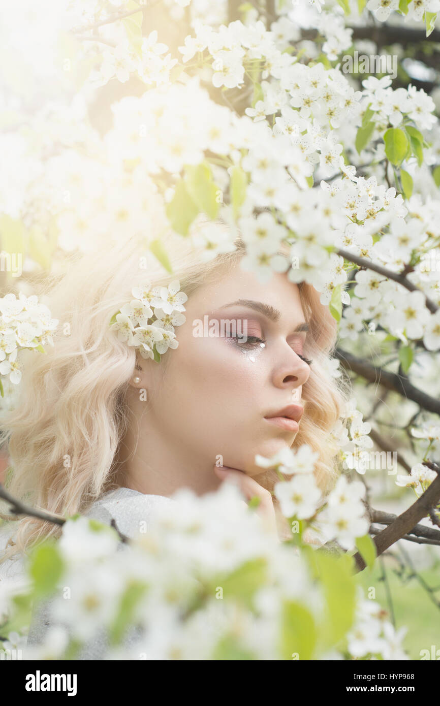 Lovely girl with curly blonde hair in spring floral garden, clear good warm day. Spring time. Stock Photo