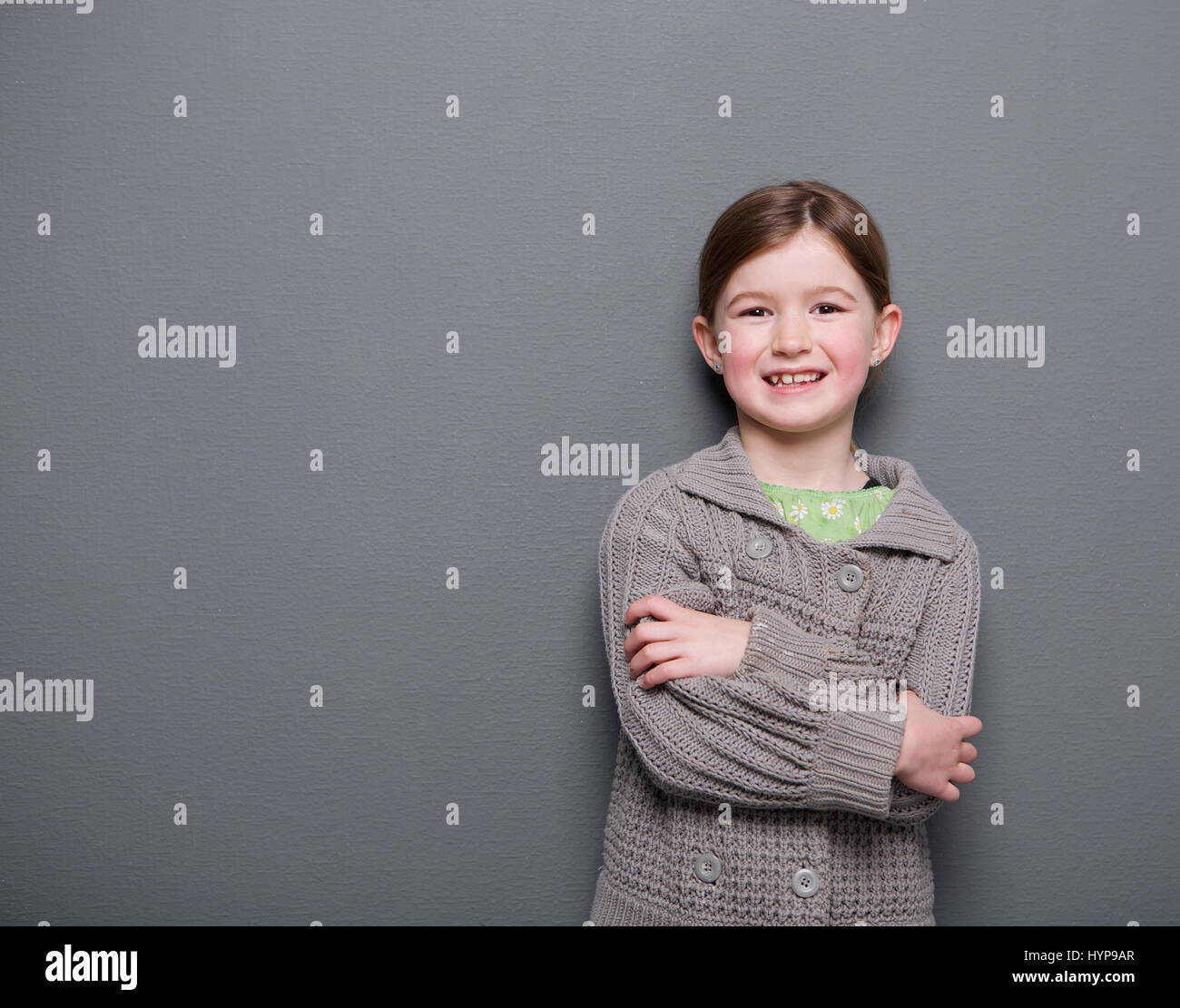 Close up portrait of a young girl smiling with arms crossed on gray ...
