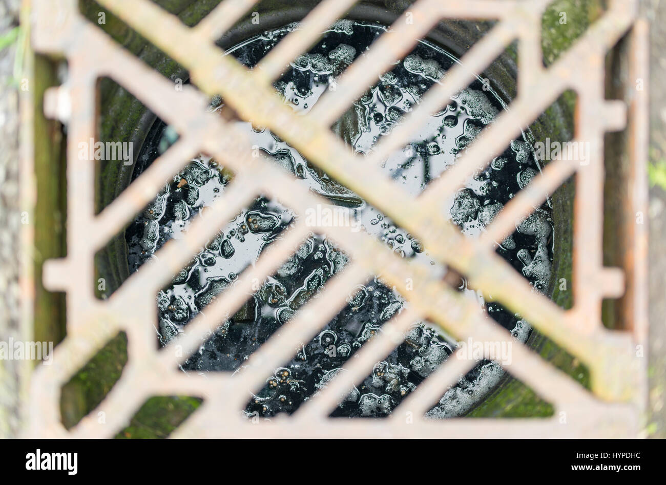 View looking down into a storm drain, with the grating out of focus, and showing wet sludge at the bottom of the drain. Stock Photo