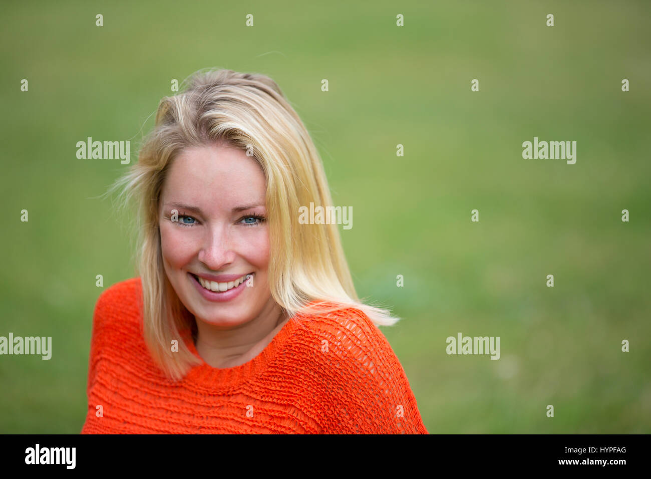 Portrait of a blonde woman sitting in the park and smiling at camera ...