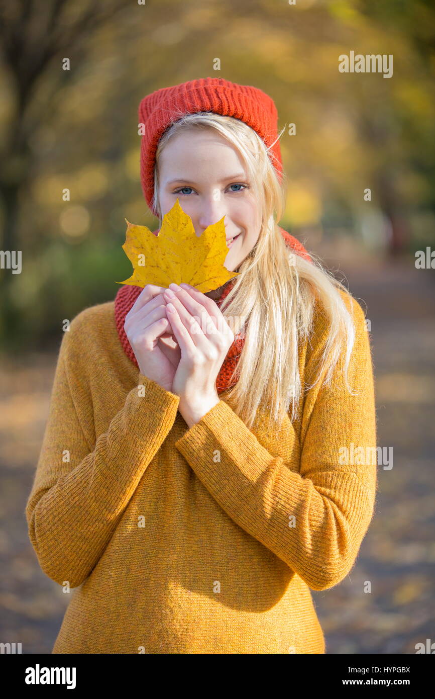 Portrait of a pretty blonde woman in park in autumn with leaf covering ...