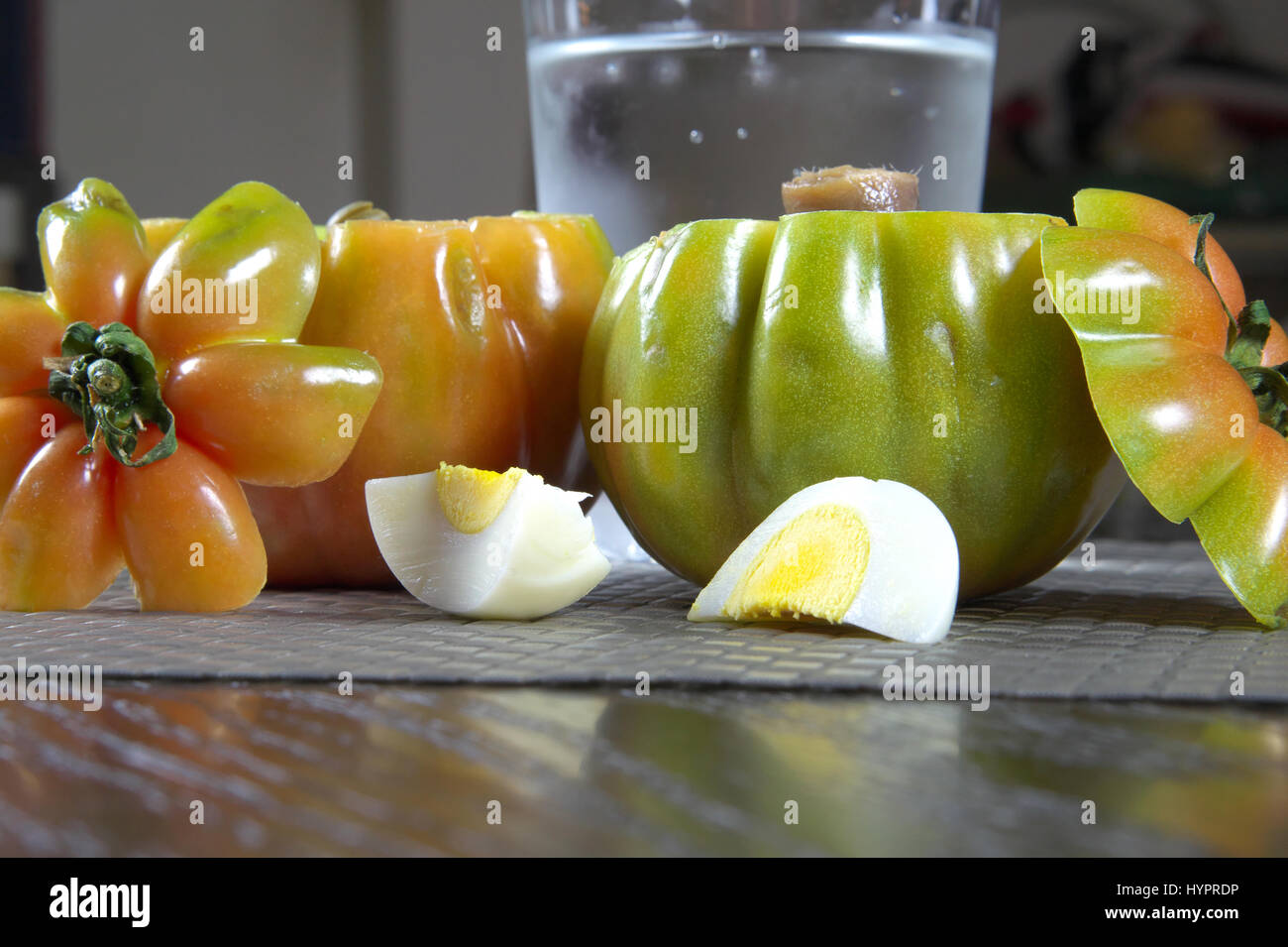 Stuffed green tomatoes on a placemat with cut boiled eggs and a glass of water in bokeh background - Still life objects and food series Stock Photo