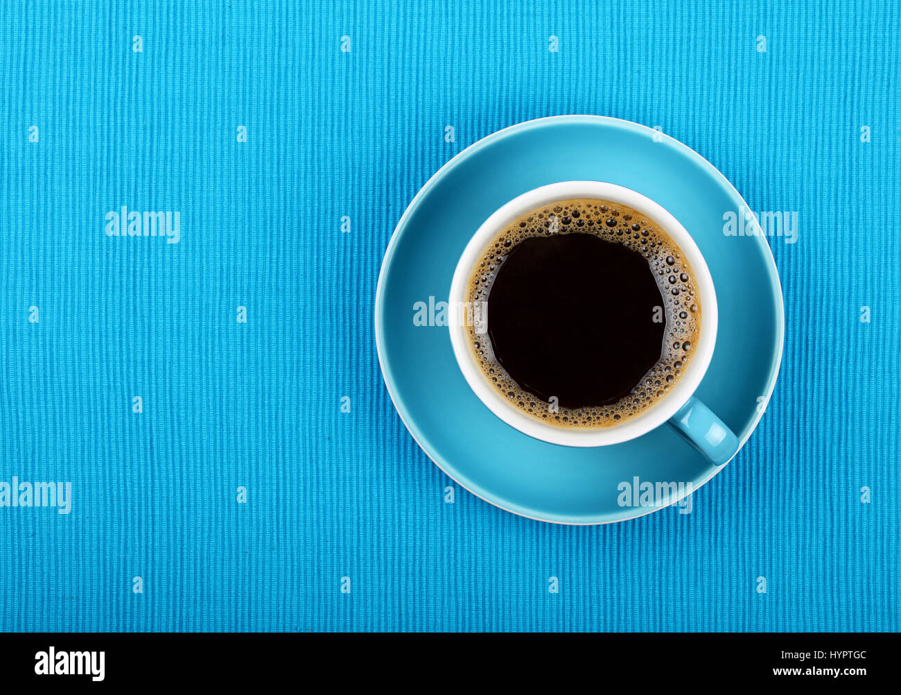Full cup of black Americano or instant coffee on saucer over blue tablecloth, close up, elevated top view Stock Photo