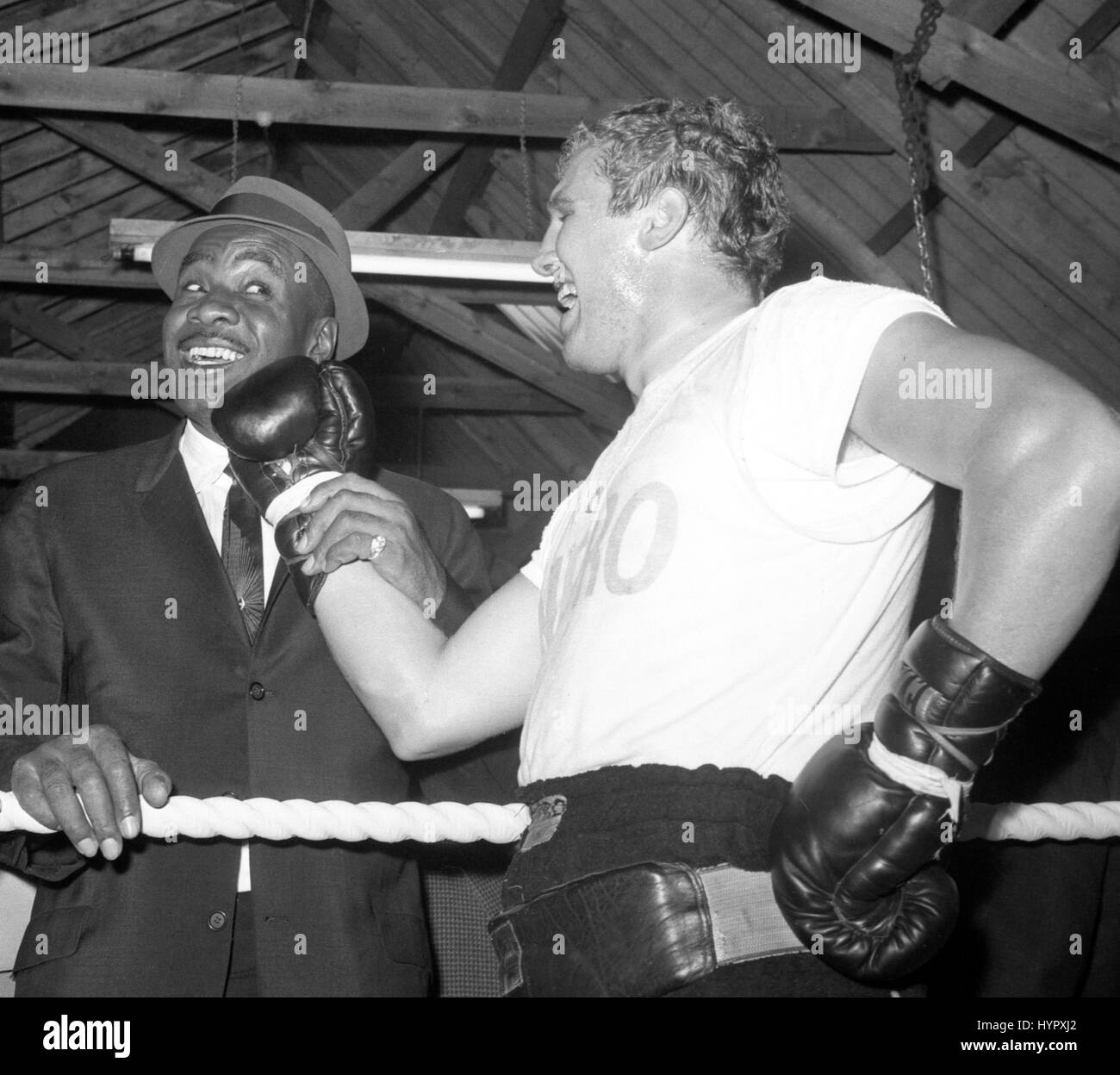 World heavyweight champion Sonny Liston (l) poses with British heavyweight Billy Walker as he plants a playful right on his jaw. Liston, paying a visit to the Pitsea, Essex, farm where Walker has his training camp, had just watched the Briton training. Stock Photo