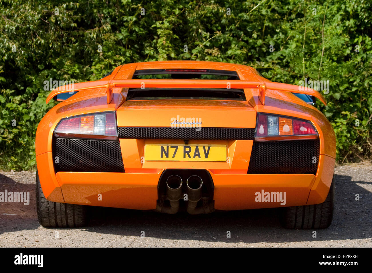 Orange Lamborghini rear view low wide sleek luxury Italian sports car parked. Twin exhaust wide wheels and tyres rear aerofoil mid v engined power. Stock Photo