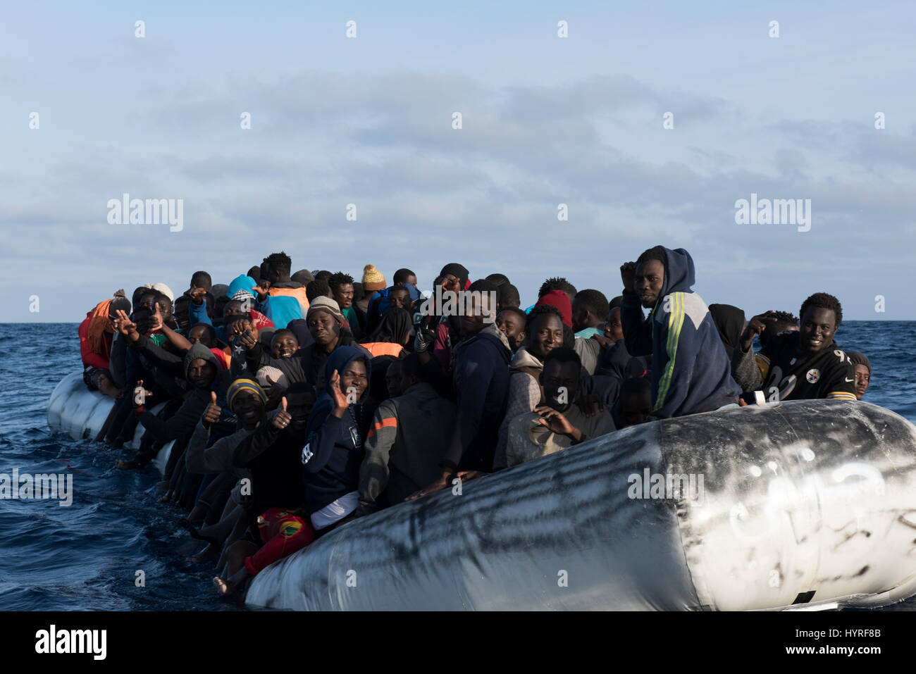 About 150 refugees/migrants from africa sitting on a rubberboat in bad condition and want to cross the mediterrean sea to europe. Stock Photo