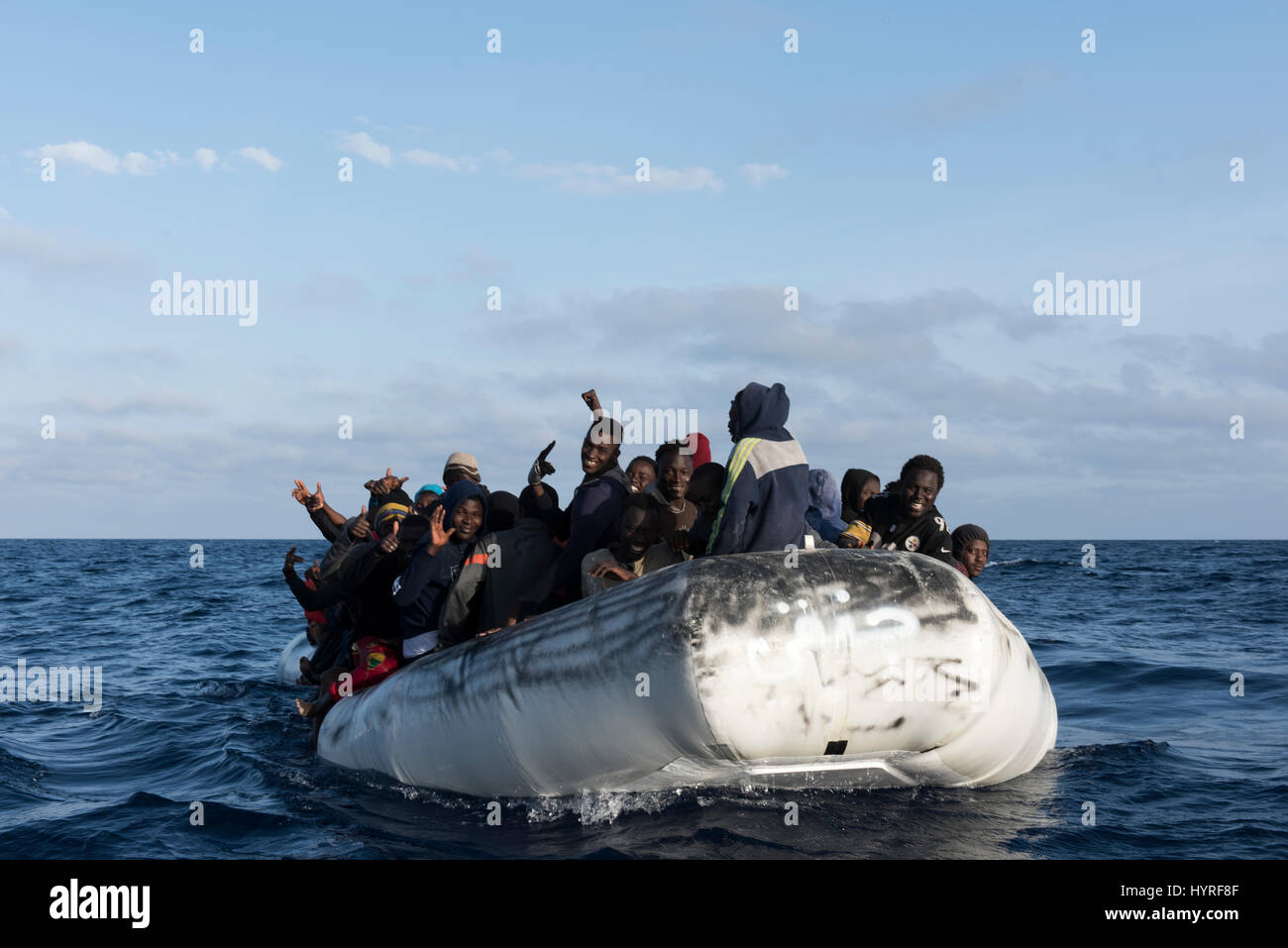 About 150 refugees/migrants from africa sitting on a rubberboat in bad condition and want to cross the mediterrean sea to europe. Stock Photo